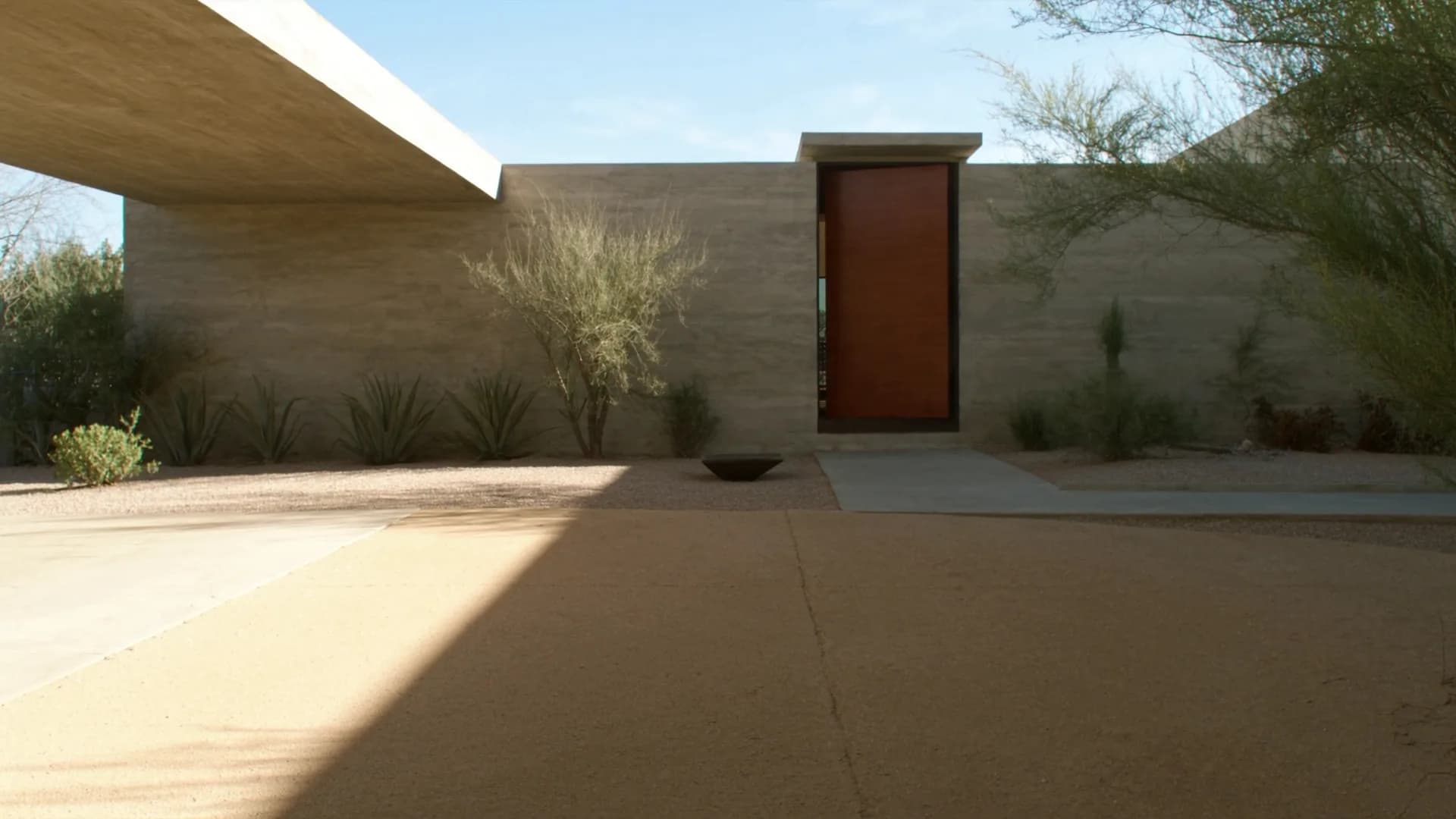 Modern desert home entrance with warm wood pivot door and desert landscaping